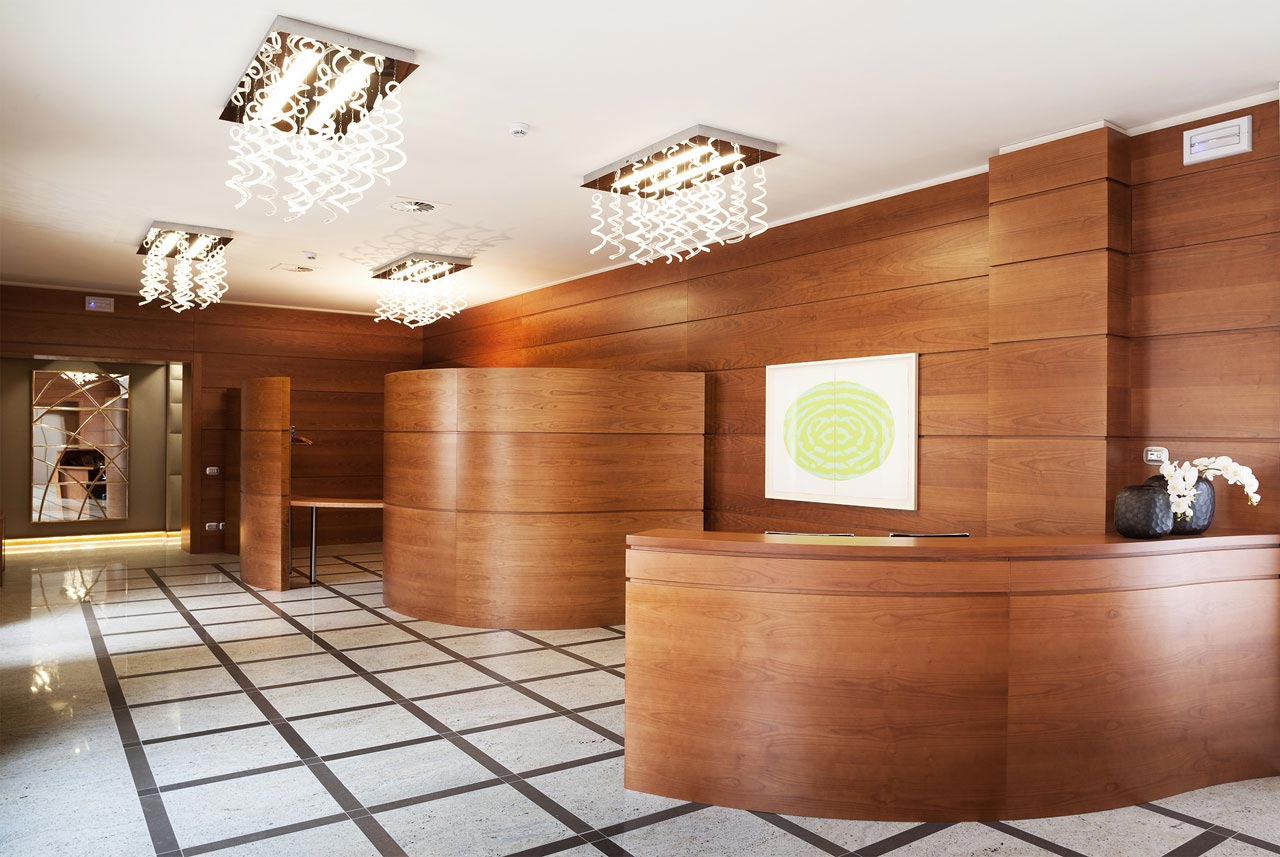 Reception aziendale moderna con front desk e pareti in legno su misura: Baggio Arredamenti.